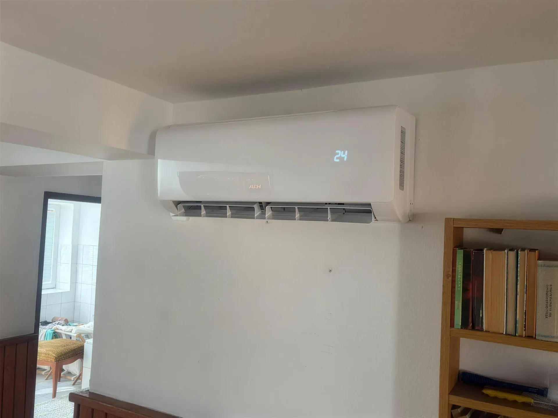 Nástenná klimatizácia AUX v izbe s knižnicou, displej ukazuje 24 °C